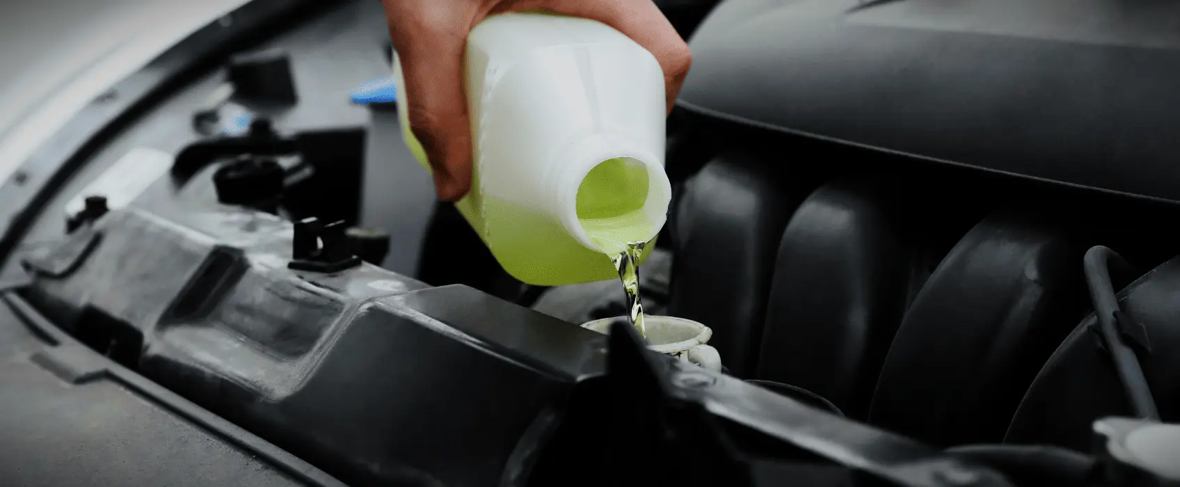Hand pouring a bottle of yellow coolant into car under hood.