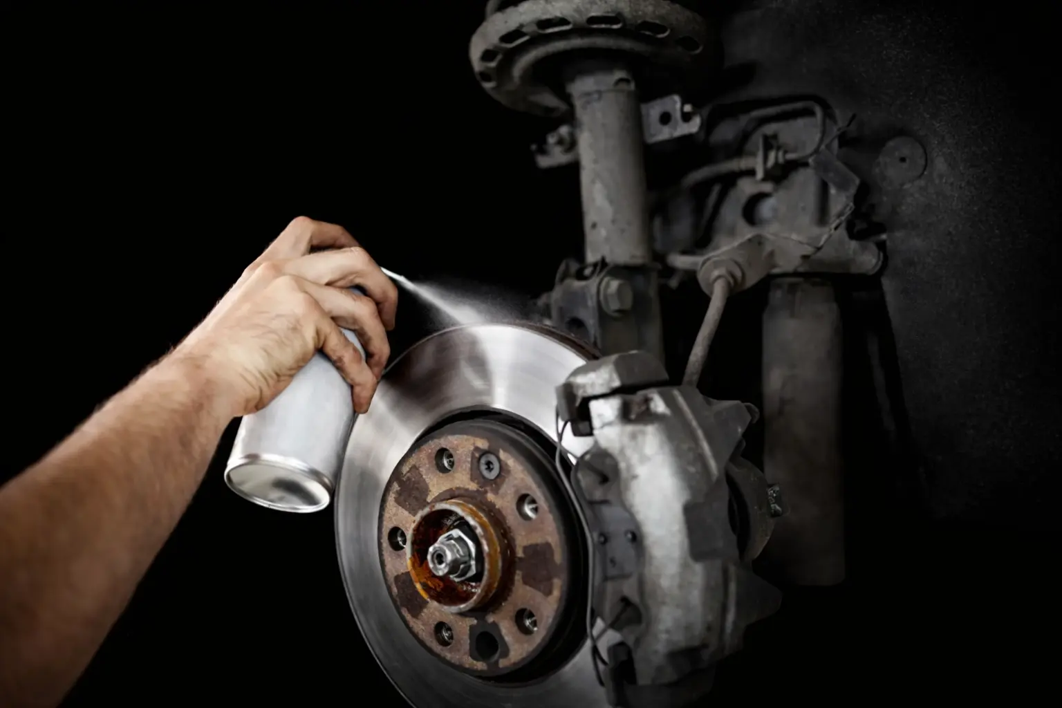 Hand spraying break cleaner on a car's open break wheel.